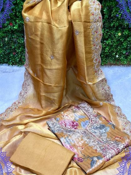 A luxurious golden-yellow unstitched suit set. The top has a digital floral print with embroidery, and the organza dupatta features a beautiful scalloped border.