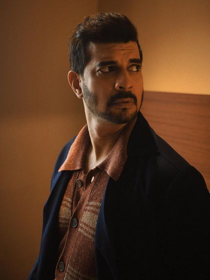 A cinematic portrait of Tahir Raj Bhasin, looking off-camera. The warm tones and focused light create a sense of intrigue and narrative.
