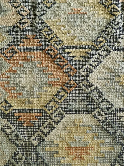A close-up of a handwoven dhurrie, showing the intricate geometric pattern and the rich, earthy color palette. These are the handwoven stories under your feet that define both comfort and style.