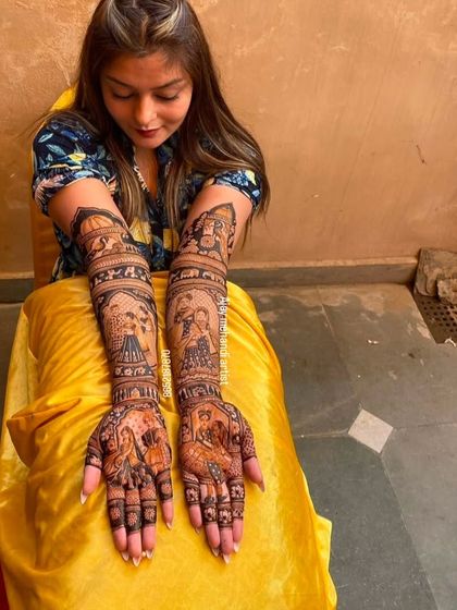 A happy client showing her full-arm and leg mehndi, featuring a mix of portraits and traditional motifs.