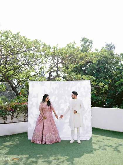 A couple stands before a simple white backdrop set up outdoors, a minimalist approach that puts all the focus on their connection and beautiful attire.