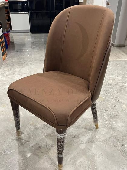 A close-up of one of my favorite dining chair designs. It features a two-tone upholstery in a rich brown, with elegant curves and tapered legs capped in brass, embodying understated luxury.