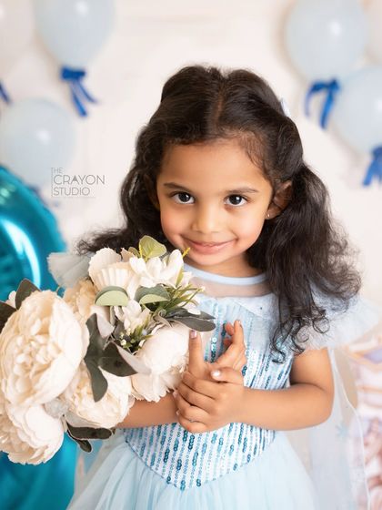 The birthday princess holds a bouquet of flowers, her gentle smile lighting up the studio.
