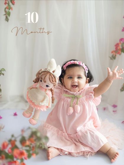 Ten months old and full of personality. This little girl is waving happily, holding her doll, in a setup filled with beautiful bougainvillea flowers.