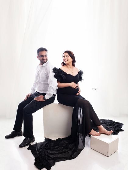 A classic seated couple pose with a twist. The back-to-back seating arrangement allows for a sweet, knowing glance between the partners, captured in a bright and airy studio.