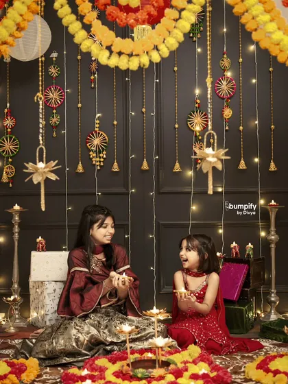 Sisters sharing a quiet moment with diyas during their festive photoshoot. The intricate backdrop and warm lighting create a truly magical scene.