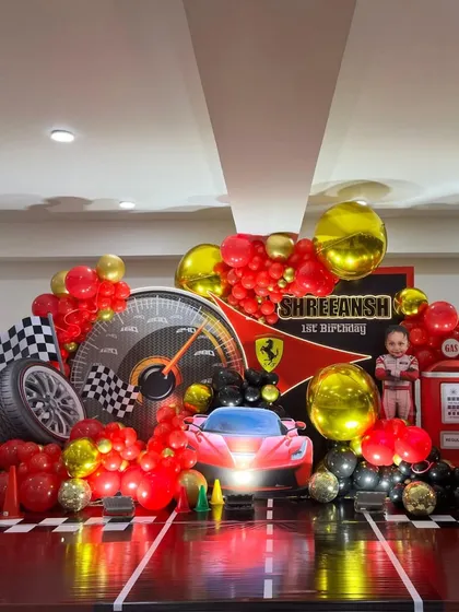 This is a full stage setup for a Ferrari car racing theme. It features a personalized backdrop, 3D car and gas pump props, and a dynamic balloon arrangement in signature red, black, and gold.