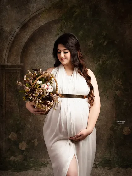 A gentle and beautiful portrait of a mom-to-be in a white gown, holding a basket of flowers. The dark, painterly background makes her stand out, creating a classic, artistic feel.