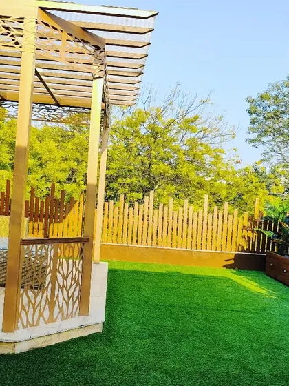 A daytime view of a stunning golden-hued pergola with laser-cut details, a slatted wood backdrop, and a comfortable wicker sofa set.
