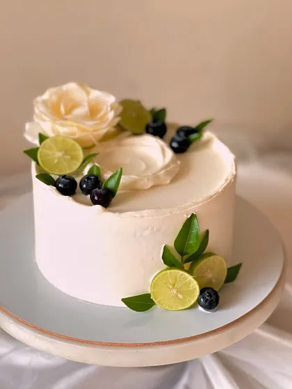 My signature Italian Lemon & Blueberry cake, presented on a stand. This design highlights the freshness of the ingredients with real blueberries, lime slices, and a delicate white flower.