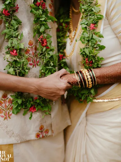 A close-up of the wedding rituals. The bride's hand, adorned with traditional bangles, rests gently over her perfectly draped Kerala saree.