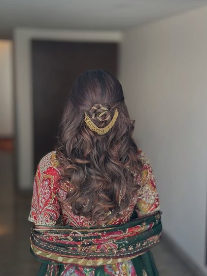 This half-up style features a beautiful rose-shaped bun created from the hair itself, held in place with a golden accessory. The rest of the hair falls in soft, beachy waves.