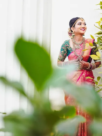 A creative shot of the bride amidst greenery, her vibrant saree and makeup standing out beautifully.