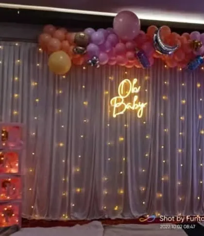 A closer view of the 'Oh Baby' neon sign against the white fairy light curtain, creating a warm and magical ambiance for the baby shower.