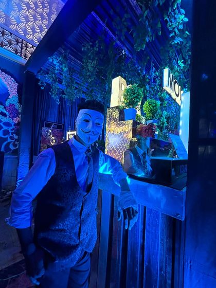 A full shot of our bartender in a Guy Fawkes mask, posing at a stylishly decorated bar. This demonstrates our commitment to creating a fully immersive, themed experience.