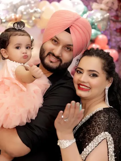 A happy family portrait of a father, mother, and their daughter at her unicorn themed first birthday party. The father is wearing a traditional Sikh turban.