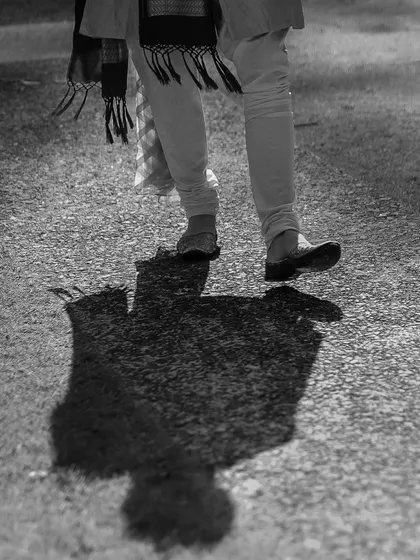 An artistic black and white shot focusing on the groom's shadow and his traditional footwear (juttis), telling a story of his journey to the wedding.
