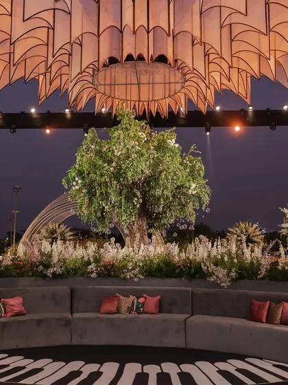 A curved grey velvet sofa faces a large tree centerpiece under a magnificent custom-built chandelier, part of the unique musical-themed reception.