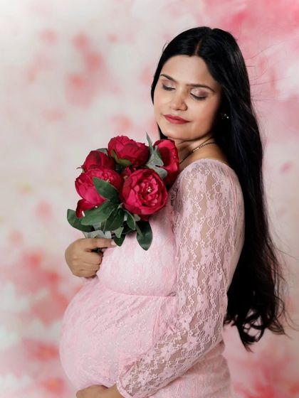 A peaceful moment captured in the studio. Holding a bouquet of red flowers, this expecting mother takes a moment to connect with her baby.