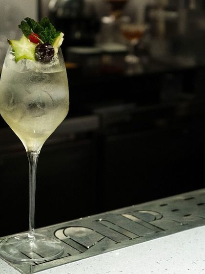 Slip into an ethereal gustatory experience with our concoctions. This elegant, starfruit-garnished spritz is served in a tall wine glass, perfect for a light and refreshing sip.