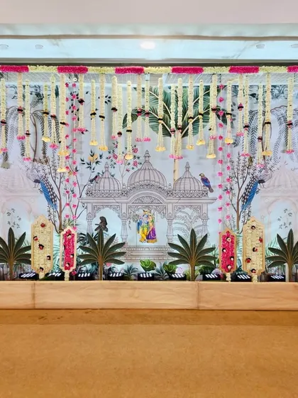 We designed this elaborate stage for a baby shower with a Vrundavan theme. The backdrop features a custom print of a temple scene with peacocks, accented by hanging floral strings in pink and white for a soft, celebratory feel.