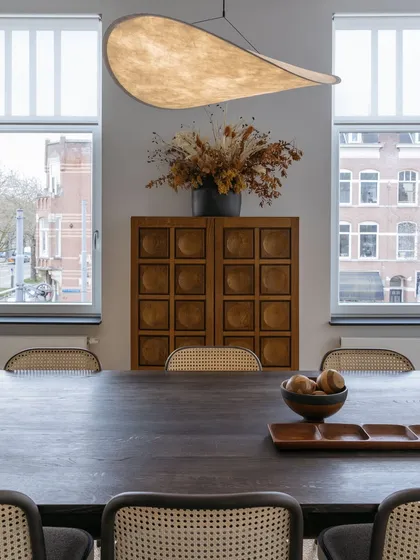 A closer view of the dining area, highlighting the sculptural pendant light and the texture of the caned chairs. The windows overlook the historic Rotterdam neighborhood, connecting the interior to its urban context.