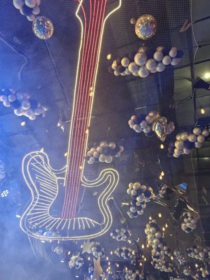 Rock on! This image shows a unique musical-themed ceiling decoration, featuring a large neon guitar and balloon "clouds." It's a perfect example of how we can transform an entire space, including the ceiling, to fit a creative theme.