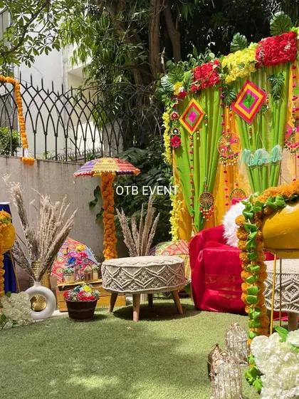 A side view showcasing the details of the outdoor Mehendi decor, including the macrame stools, marigold-wrapped stands, and colorful backdrop hangings.