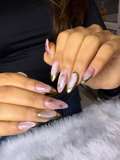 This design is pure luxury. It features a soft pink and white marbled base with brilliant gold chrome tips and delicate, hand-painted gold starbursts.