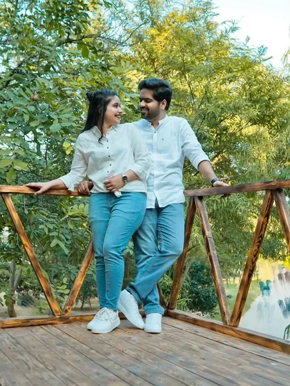 A relaxed portrait of the couple on a wooden deck surrounded by lush greenery. Their matching white shirts and jeans give the shoot a casual, "everyday love" feel.