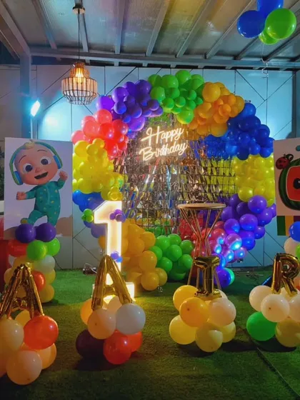 A bright and colorful Cocomelon theme for a first birthday. The setup includes a rainbow balloon arch, character cutouts, and the birthday boy's name in balloon letters.