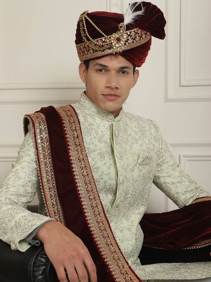 A seated portrait in a mint green sherwani with a contrasting maroon velvet shawl. This combination of colors and textures creates a look of sophisticated grace, ideal for a winter wedding.