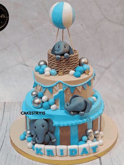 A fun three-tier elephant-themed cake for a first birthday. This 3kg chocolate cake features cute fondant elephants, one of which is riding in a hot air balloon.