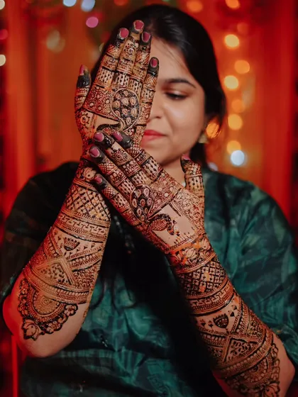 The bride proudly displays her elaborate bridal mehndi, which covers her hands and arms in beautiful, traditional patterns.