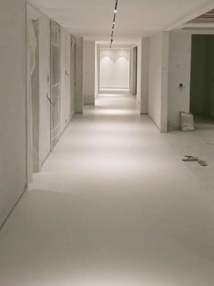 A view down the corridor with the new microconcrete floor. The track lighting is in, highlighting the flawless, uniform surface that flows through the space.