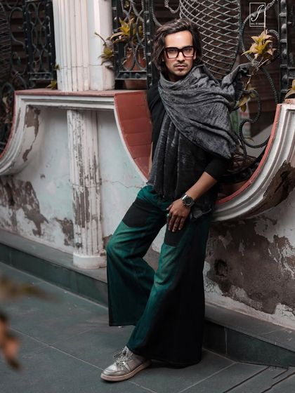 A winter fashion shoot on the street. The model's layered look with a scarf is complemented by the rustic, textured wall behind him.