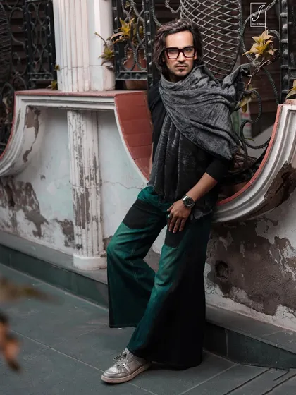 A winter fashion shoot on the street. The model's layered look with a scarf is complemented by the rustic, textured wall behind him.
