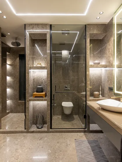 A full view of a modern bathroom, showcasing the floating vanity, back-lit mirror, and the glass-enclosed shower and toilet stalls. The grey-toned wardrobe doors on the left provide ample storage.