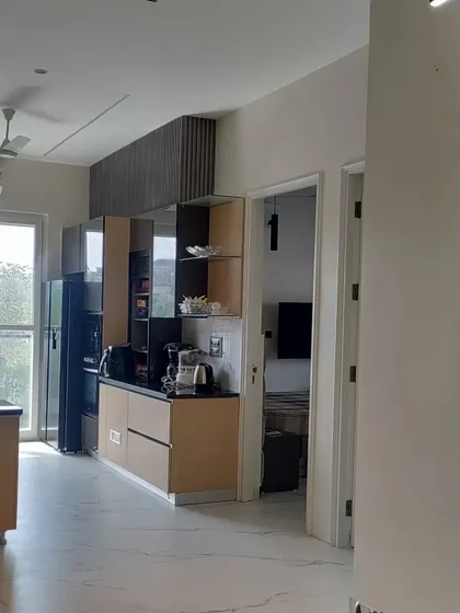 An open-plan concept in a Noida residence, where the kitchen and pantry area are seamlessly integrated with the living space. The design uses a combination of wood-finish and dark cabinets for a modern, functional kitchen.