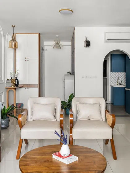 A bright and airy living space where classic arches and modern furniture coexist. The two cream-colored armchairs create a cozy conversation spot, while the view extends towards the foyer and kitchen, showing the home's cohesive design.