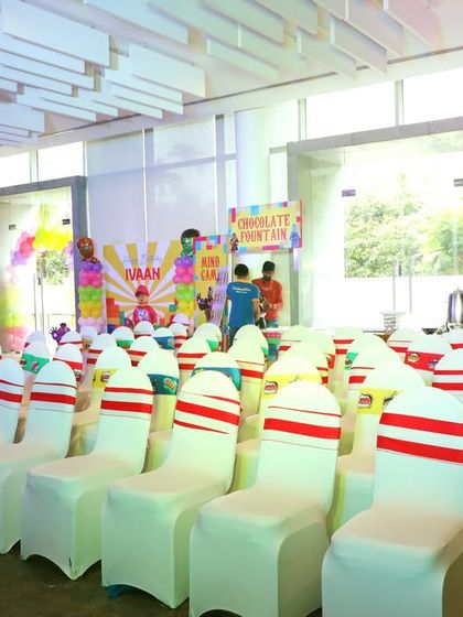 The seating arrangement for a party, with chairs neatly lined up facing the stage. The chair covers are tied with colorful sashes to match the event's theme.
