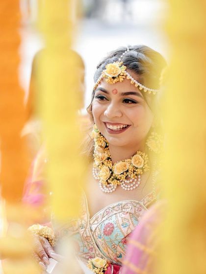 A beautiful, candid shot of the bride smiling during her Haldi ceremony. Framed by yellow marigold garlands, her happiness and floral jewelry are the focus of this lovely portrait.
