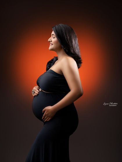 A classic profile shot in a timeless black gown. The warm back-light creates a beautiful halo effect, highlighting the silhouette of the mother-to-be.