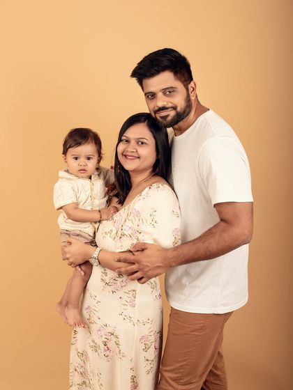 A beautiful first family portrait in the studio. The coordinated neutral outfits and the parents' loving gaze on their baby create a warm and connected image.