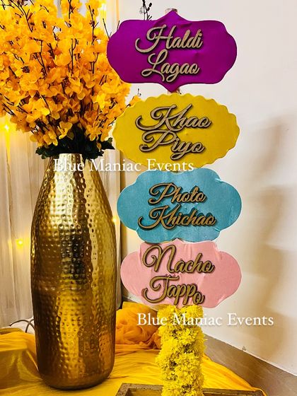 Fun and colorful props are a must for any Haldi. This image shows a set of custom signs and a vase of yellow flowers, ready for a fun-filled event.