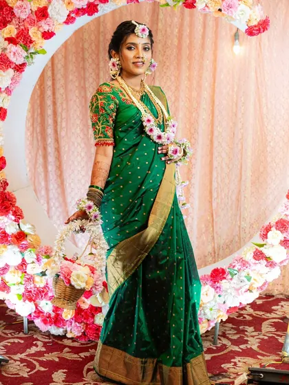 A full-length photo of the mom-to-be at her baby shower event, standing gracefully in front of a floral backdrop that complements her mehendi.