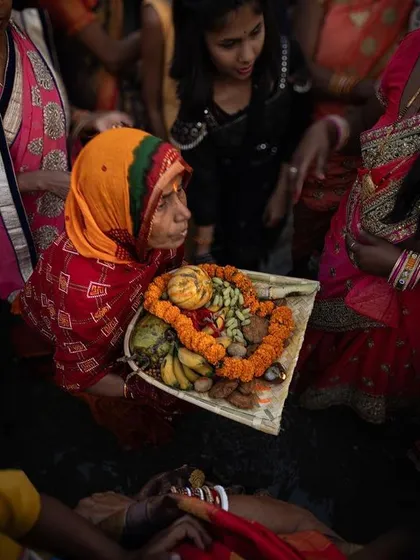 An overhead view shows a woman carrying a tray of offerings through a crowd, a key part of the Chhath Puja ceremony.