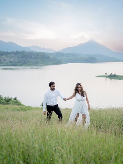 A romantic pre-wedding photo of a couple walking hand-in-hand through a field with a lake and mountains in the background. This showcases my ability to shoot in stunning destination locations.
