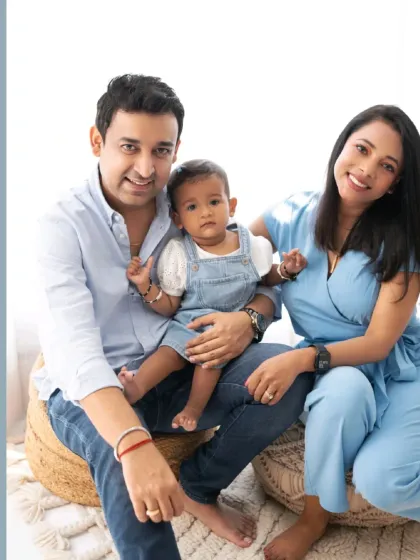A classic portrait of a family of three, smiling warmly for the camera. The coordinated blue and white outfits create a clean and cohesive look.