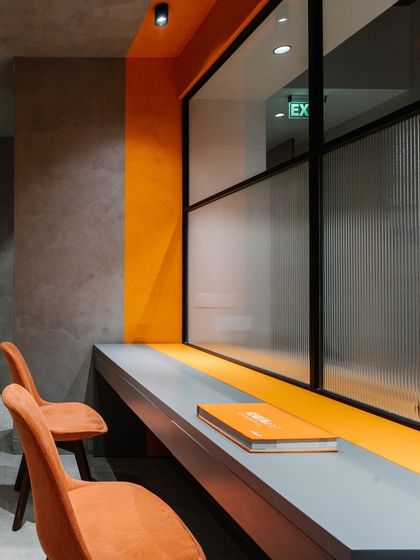 A study nook in the basement, featuring an orange accent wall and a long desk overlooking the lounge area. The fluted glass provides a degree of separation without full enclosure.